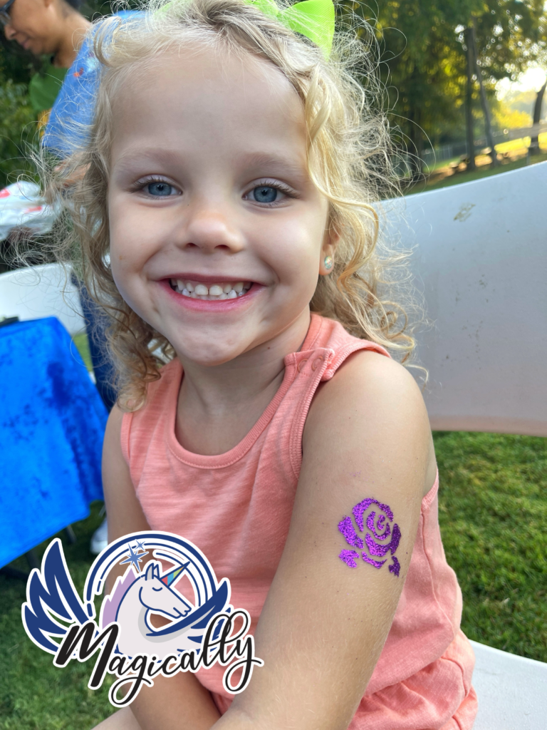 Happy girl smiling with a sparkling glitter tattoo on her arm, showcasing a fun and colorful design.